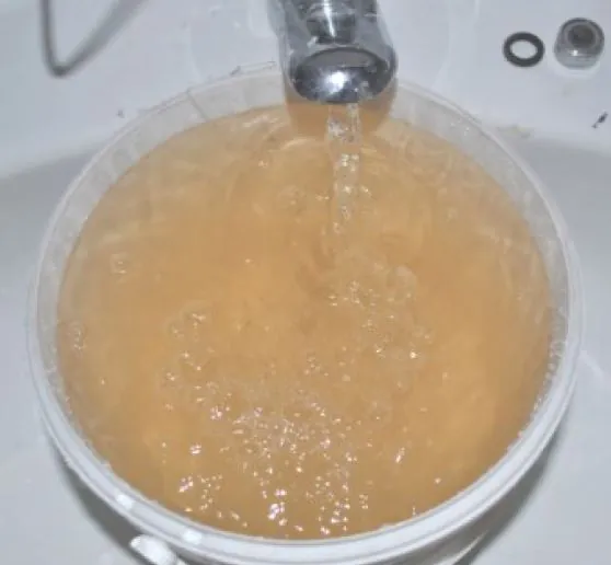 Ein Glas unter dem Wasserhahn, gefüllt mit deutlich braun gefärbtem Leitungswasser